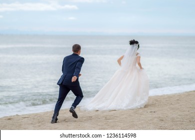 Sea Wedding Walk. 
Happy Bride And Groom Run Along The Seashore