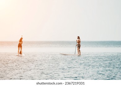 Sea woman and man on sup. Silhouette of happy young woman and man, surfing on SUP board, confident paddling through water surface. Idyllic sunset. Active lifestyle at sea or river. - Shutterstock ID 2367219331