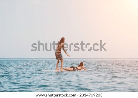 Sea woman and man on sup. Silhouette of happy young woman and man, surfing on SUP board, confident paddling through water surface. Idyllic sunset. Active lifestyle at sea or river. Slow motion