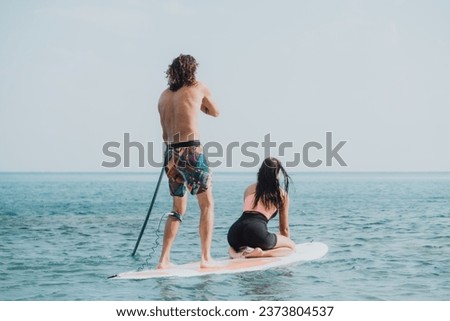 Sea woman and man on sup. Silhouette of happy young woman and man, surfing on SUP board, confident paddling through water surface. Idyllic sunset. Active lifestyle at sea or river.