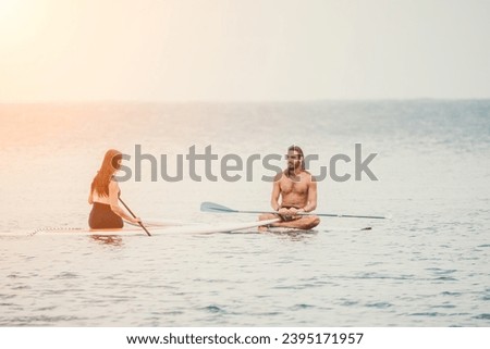 Sea woman and man on sup. Silhouette of happy young woman and man, surfing on SUP board, confident paddling through water surface. Idyllic sunset. Active lifestyle at sea or river.