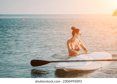 Sea woman sup. Silhouette of happy middle aged tanned woman in rainbow bikini, surfing on SUP board, confident paddling through water surface. Idyllic sunset. Active lifestyle at sea or river. - Powered by Shutterstock