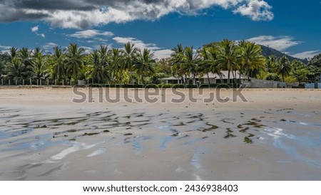 The seabed was exposed at low tide. Streams, puddles of water on the sand. Cottages are visible on the shore, among palm trees.  Clouds in the blue sky. Madagascar. Nosy Be  