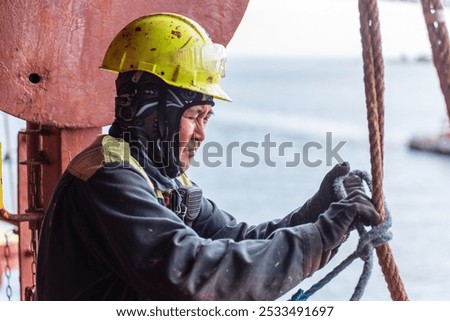 Seafarer securing a rope to a fitting, focused on safely preparing the pilot ladder. The tension in the hands reflects the importance of precision and safety in this critical task.