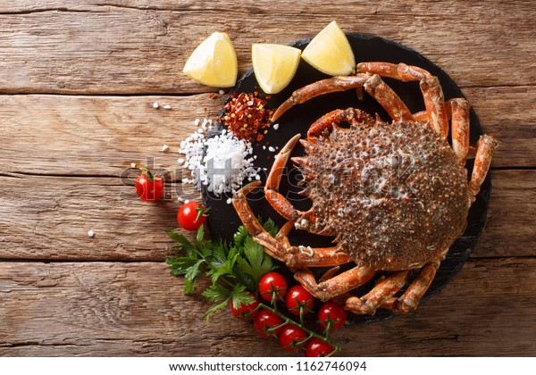 Seafood background: raw edible spider crab with\
ingredients close-up on a stone board on a wooden table. horizontal\
top view from above\
