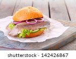 Seafood burger with a freshly baked crusty bun, fillet of fish, onion and lettuce served on a rustic wooden board