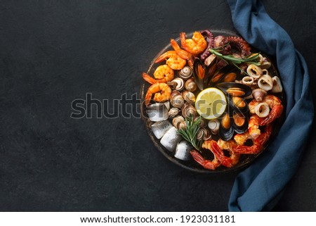 Seafood charcuterie platter board with shrimp, oysters, fish and octopus on black background and free space