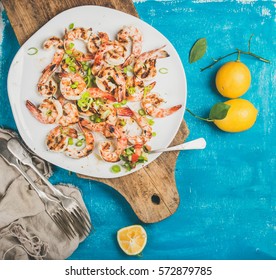 Seafood dinner. Grilled tiger prawns in white plate with lemon, leek and chili pepper on wooden board over bright blue background, top view, copy space. Slow food concept - Powered by Shutterstock