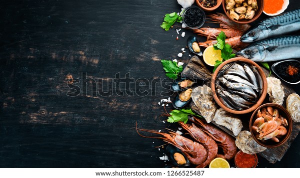 Seafood. Fresh\
fish, shrimp, oysters and caviar on a black wooden background. Top\
view. Free copy space.