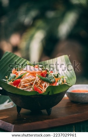 seafood green papaya salad (Som Tam) , Thai food, in banana leaf dish on traditional mat decorating with ingredients such garlic, shallot, papaya, tomato, cow pea, Fermented Rice Flour Noodles, sticky