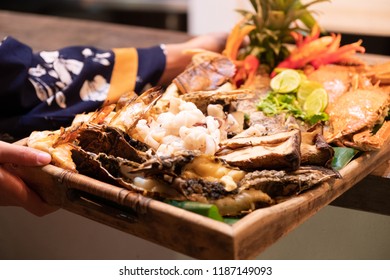 Seafood grilled (crab, fish, shrimp and shell bbg) on a wooden plate served by woman with bohemian dress costume.