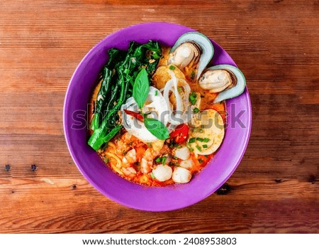 seafood laksa soup with shrimp, prawn, sea shell, noodles and boiled egg served in dish isolated on wooden table top view of hong kong food