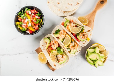 Seafood. Mexican food. Tortilla tacos with traditional homemade salsa salad, parsley, fresh lemon, avocado and grilled shrimp pawns. On a white marble background. Top view copy space