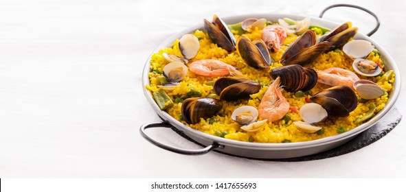 Seafood Paella, famous Spanish  rice dish in traditional frying pan. Paella valenciana with pink prawns, clams and mussels on saffron rice with vegetables.