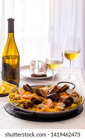 Seafood Paella, famous Spanish  rice dish in traditional frying pan served with white wine. Paella valenciana with pink prawns, clams and mussels on saffron rice with vegetables.