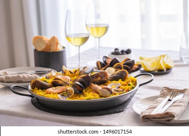 Seafood Paella with  prawns, clams, mussels on saffron rice and vegetables and  bottle of white wine on restaurant table.