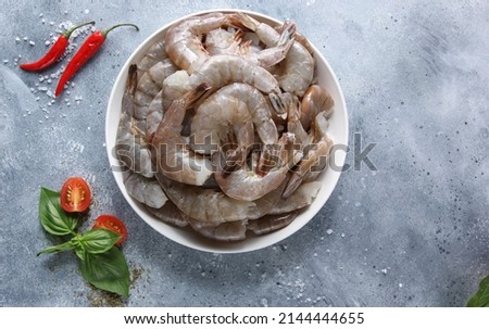 Seafood. Raw green prawns shrimp on a white plate with basil, chili peppper, spices  on a light grey background. Flatlay, top view. Background image, copy space 