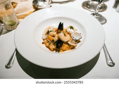 A seafood risotto dish topped with shrimp, mussels, clams, and squid, garnished with parsley, served on a white plate with a creamy texture and vibrant presentation.