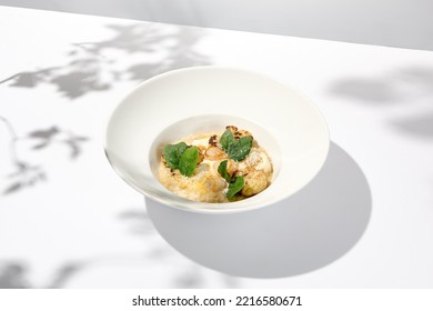 Seafood Risotto With Scallops And Cauliflowers On White Plate. Creamy Risotto With Sea Scallops And Cauliflowers. Italian Risotto With Sea Scallops On Light Background With Shadows Of Leaves.