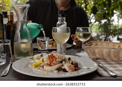 Seafood salad on a table. Outdoor restaurant in Italy. White wine, water, bread, and olive oil create an atmosphere of taste and relaxation. - Powered by Shutterstock - Get 15% off with code: PIKWIZARD15