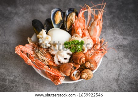 Seafood shrimps prawns squid mussels spotted babylon shellfish crab  on plate and dark background / Cooked food served seafood buffet concept 