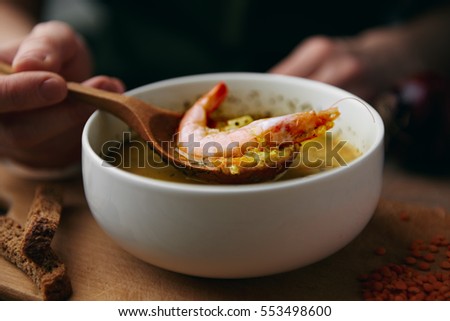 Seafood soup. Macro shot of woman holding wooden spoon with shrimp.