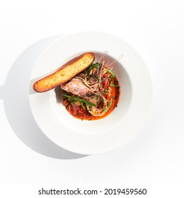 Seafood With Tomato Sauce On White Restaurant Plate. Shrimp Seafood And Tomato Stew Garnished With Fried Bread. Isolated On White Background