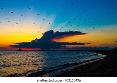 Seagulls fill the sky as the sun sets behind a thunderhead storm cloud over Lake Michigan at the Grand Haven, Michigan, pier and lighthouse
