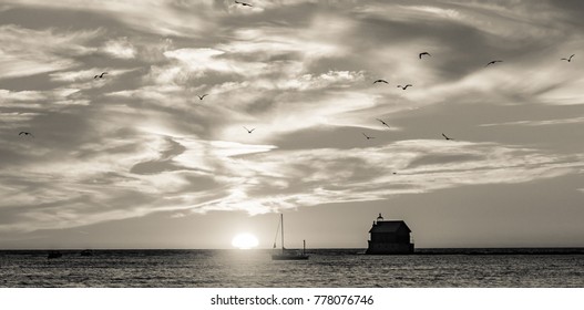 Seagulls fly over Lake Michigan as the sun sets behind the lighthouse pier in Grand Haven, Michigan