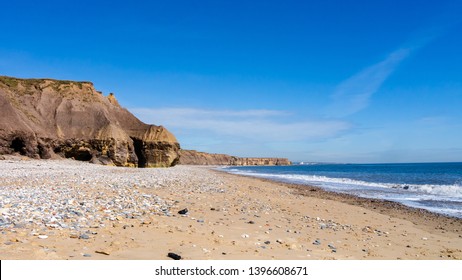 Seaham Hall Beach in County Durham with cliffs off to the left, golden sand and calm sea to the right. Taken on a warm sunny day with a blue sky.
