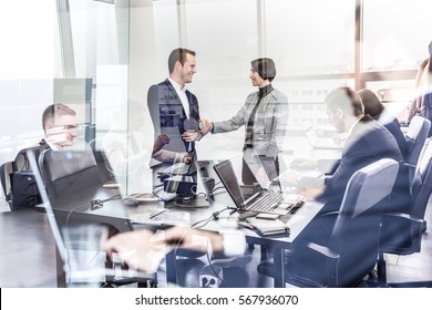 Sealing A Deal. Business People Shaking Hands, Finishing Up Meeting In Corporate Office. Businessmen Working On Laptop Seen In Glass Reflection. Business And Entrepreneurship Concept.