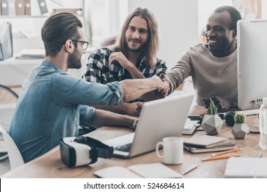 Sealing A Deal. Three Young People Having A Business Meeting In Office While Two Men Shaking Hands And Smiling