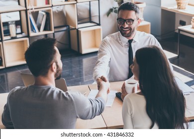 Sealing a deal. Top view of two men sitting at the desk and shaking hands while young woman looking at them and smiling  - Shutterstock ID 431846332