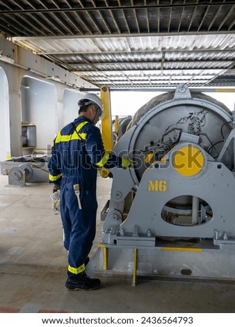 Seaman crew member of cargo vessel  equipped with personal protective equipment is doing maintenance painting of mooring winch on aft station