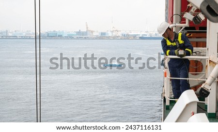 Seaman crew member of cargo vessel  equipped with personal protective equipment operate life boat davit  on the cargo ship in helmet with walkie talkie.