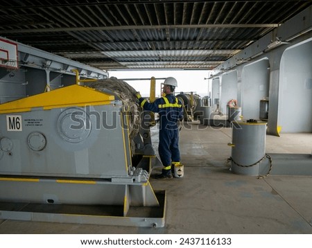 Seaman crew member of cargo vessel  equipped with personal protective equipment is doing maintenance painting of mooring winch on aft station