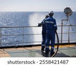 Seamen during fire emergency training drill, on board a merchant cargo ship, wearing fire fighting equipment and helmets. Rigged fire hose for jet spray, with emergency fire pump.