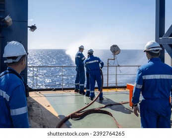 Seamen during fire emergency training drill, on board a merchant cargo ship, wearing fire fighting equipment and helmets. Rigged fire hose for jet spray, with emergency fire pump.