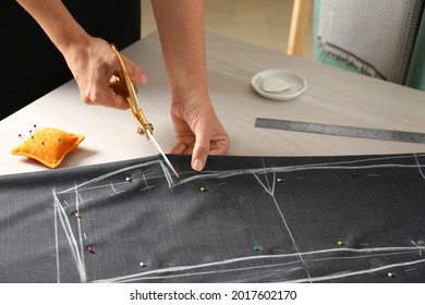 Seamstress Cutting Fabric Following Chalked Sewing Pattern At Table In Workshop, Closeup