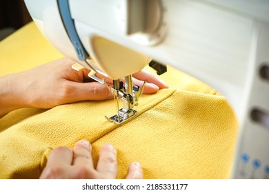 Manos femeninas de la costura sujetando y cosiendo tela amarilla en máquinas modernas de coser en el lugar de trabajo. Proceso de coser, tapicería, ropa, reparación, DIY. Concepto de pequeñas empresas hecho a mano, de hobby