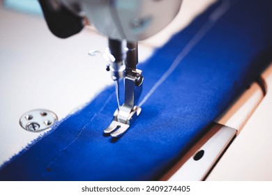 Seamstress female hands holding and stitching blue textile fabric on modern sewing machine at workplace. Sewing process, upholstery, clothes, repair, DIY. Handmade, hobby, small business concept