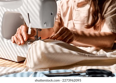 Seamstress sewing linen fabric on sewing machine in small studio. Fashion atelier, tailoring, handmade clothes concept. Slow Fashion. Conscious consumption.
