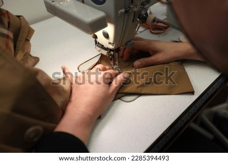 a seamstress sewing on a trench coat using a industrial sewing machine