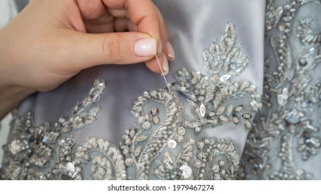 The seamstress or tailor sews beads and lace to the fabric with needle. Sewing process. Close up. Preparation for the fashion collection show.