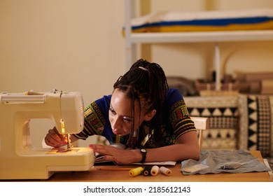 Seamstress threading sewing machine needle when working in her studio