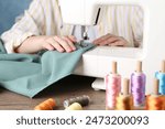 Seamstress working with sewing machine at wooden table indoors, closeup