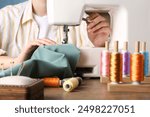 Seamstress working with sewing machine at wooden table indoors, closeup