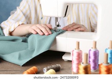 Seamstress working with sewing machine at wooden table indoors, closeup - Powered by Shutterstock