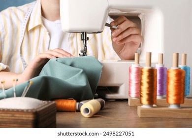 Seamstress working with sewing machine at wooden table indoors, closeup