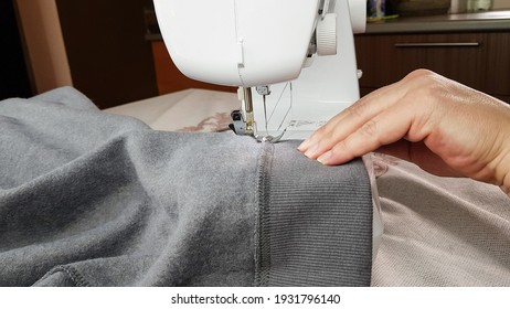 A Seamstress Works On A Sewing Machine. Women's Hands Hold The Gray Fabric And Make A Straight Stitch On It.